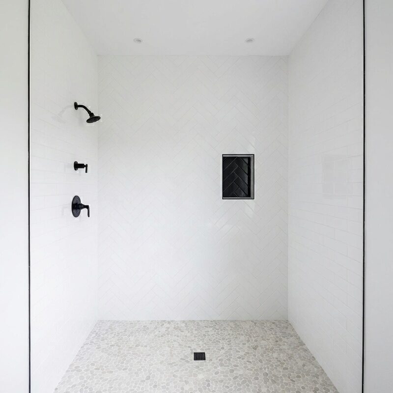 White herringbone tile shower with pebble stone floor and black fixtures, installed by BM Pro Construction